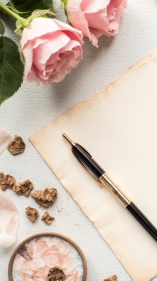 Photograph of a vintage paper letter with a pen, rose petals, and chocolates in soft pastel colors Wallpaper